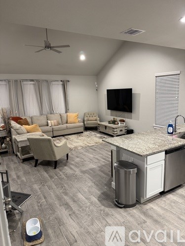 A modern living room with a grey sofa set, a television, and a kitchenette.