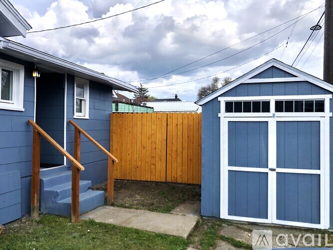 A blue house with a wooden fence and a small shed.