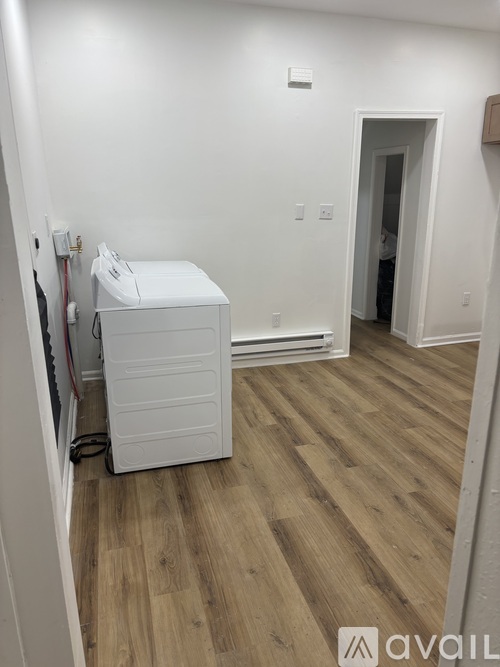 A white toilet is in a room with wooden floors and white walls.
