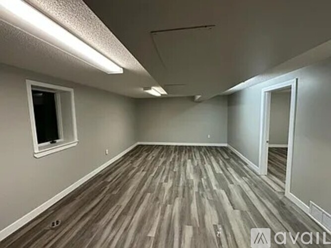 A room with wooden flooring and a window on the left wall.