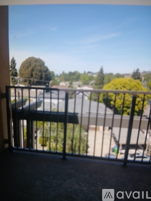 A balcony with a metal railing overlooks a parking lot and trees.