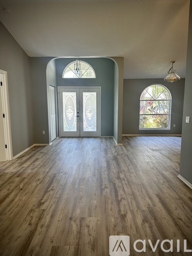A room with wooden flooring and a large arched window.