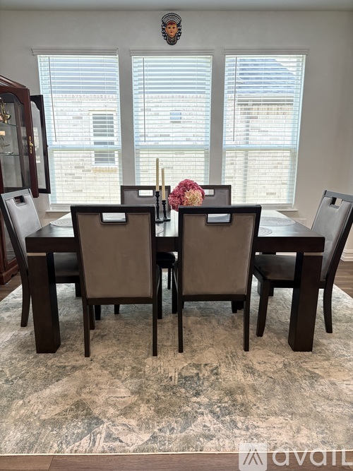A brown dining table with four chairs and a vase of flowers on top.