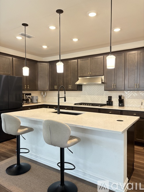 A modern kitchen with a white island and black bar stools.