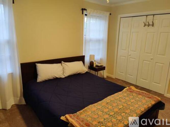 A bedroom with a bed, a nightstand with a lamp, and a window with curtains.