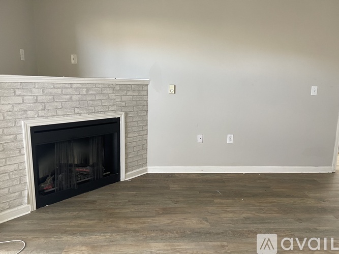 A room with a white brick fireplace and wooden flooring.