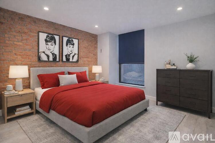 A bedroom with a red bedspread and a brick wall.