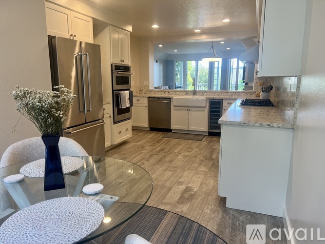 A modern kitchen with a glass table and a vase of flowers.