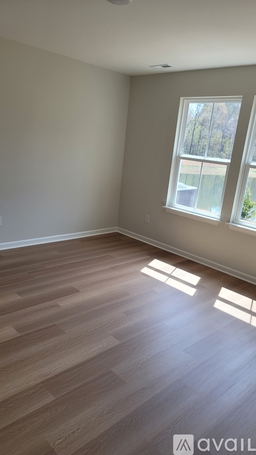 A room with wooden flooring and a window letting in sunlight.