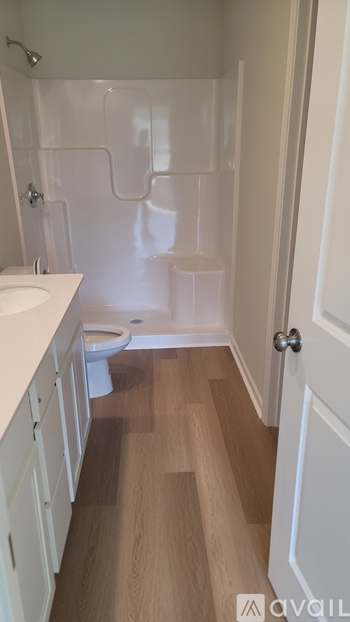 A white toilet sits in a bathroom with wood floors and white walls.