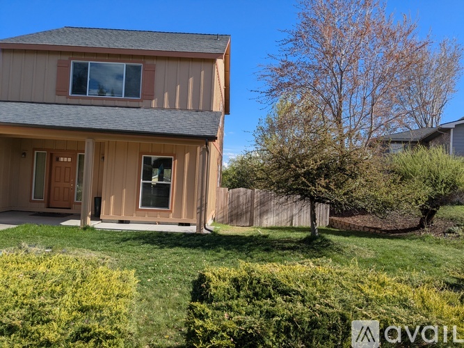 A house with a brown and beige exterior is surrounded by a green lawn and a leafless tree.