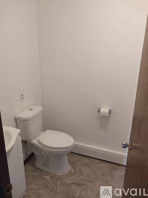 A white toilet in a bathroom with a white wall and a wooden door.