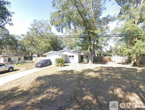 A house with a car parked in front and trees surrounding it.