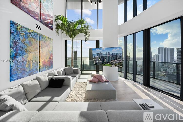 A modern living room with a large grey sofa and a view of the city through the windows.