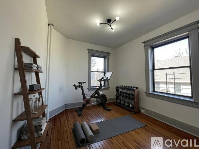 A room with a wooden floor, a ladder, a yoga mat, a bike, and a set of dumbbells.