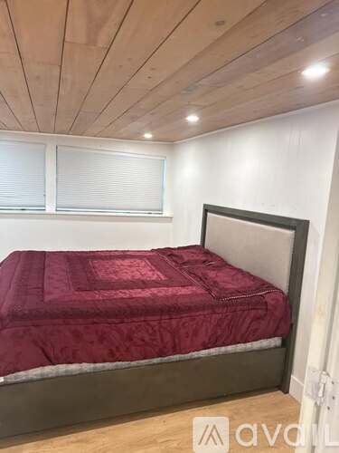 A bed with a red cover and wooden headboard is in a room with a wooden ceiling.