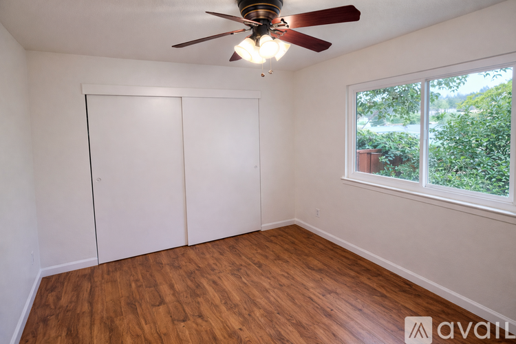 A room with a ceiling fan and a window overlooking a green area.