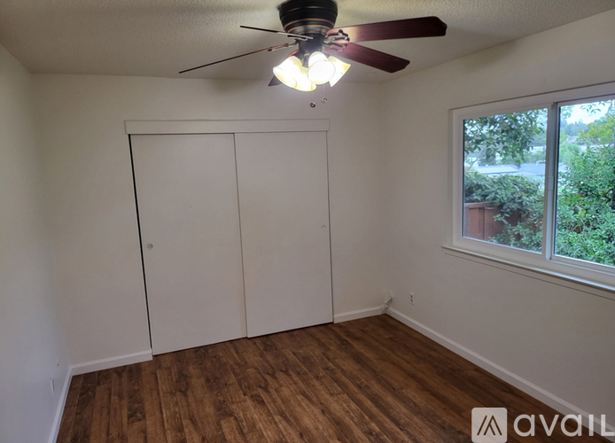 A room with a ceiling fan and a window overlooking a garden.
