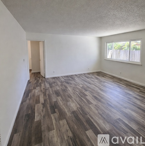 A room with wooden flooring and a window with a view of a fence.