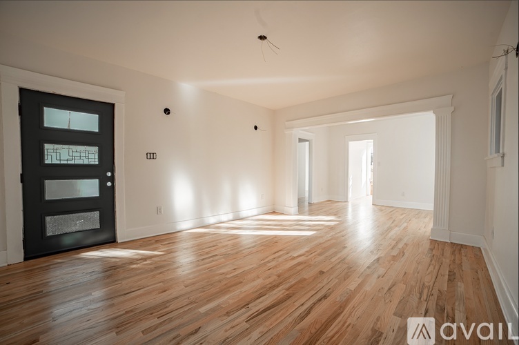 A spacious room with wooden flooring and a black door with a window.