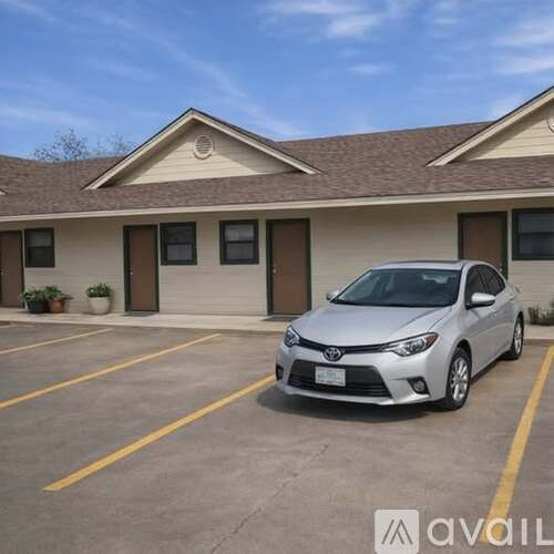 A silver Toyota car is parked in a parking lot in front of a building.