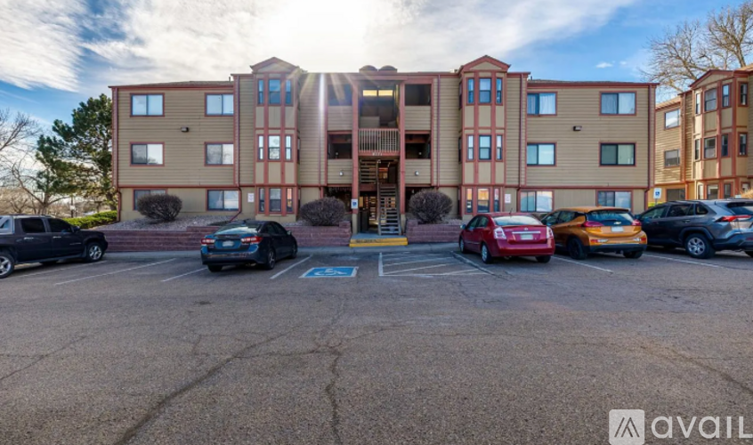 A parking lot in front of a multi-story apartment building with cars parked.