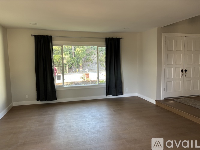 A room with a large window and a door is available for rent.