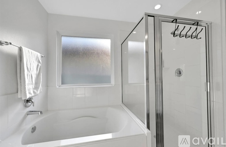 A white bathroom with a glass shower door and a white bathtub.