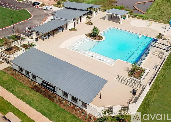 A swimming pool is surrounded by a covered area and a grassy field.