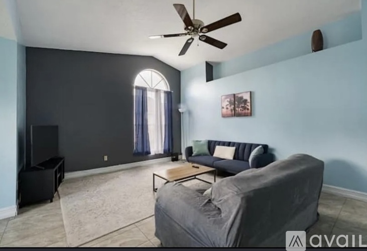 A living room with a grey couch, a black speaker, and a ceiling fan.