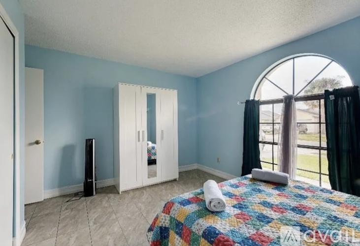 A bedroom with a bed, a window with curtains, and a television.