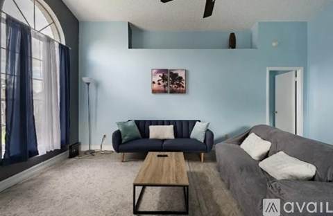 A living room with a grey couch, a blue sofa, a wooden coffee table, and a painting on the wall.