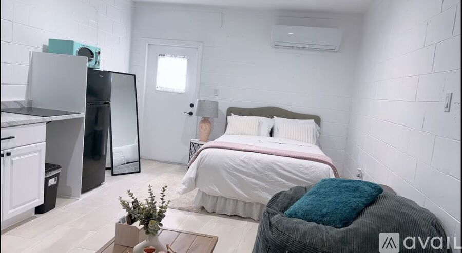 A bedroom with a bed, chair, and a small kitchenette.