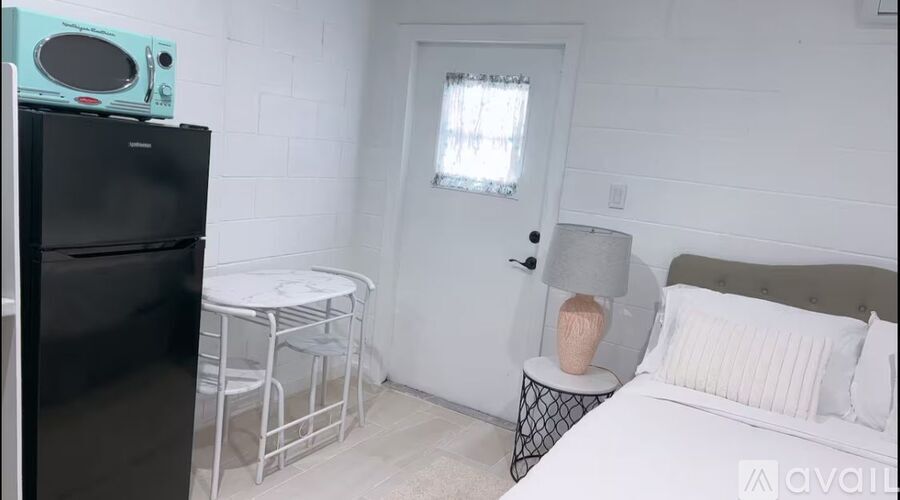 A small bedroom with a bed, table, and a refrigerator.