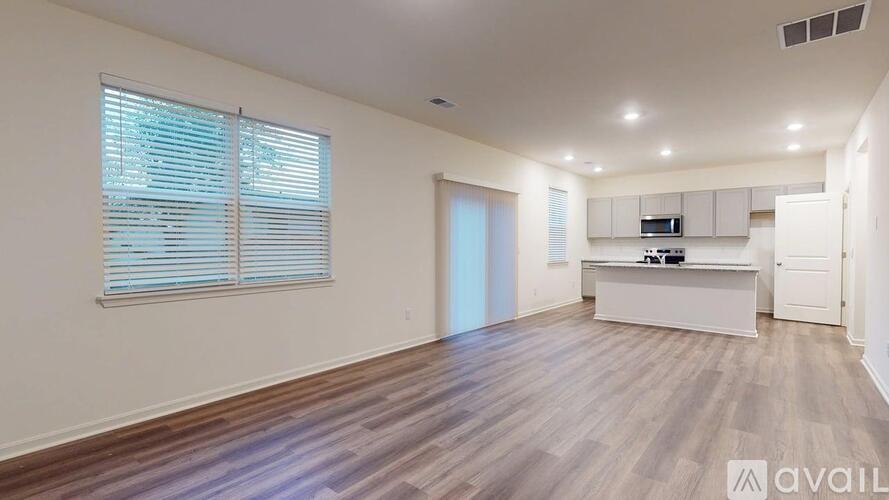 A spacious room with wooden flooring and a window with blinds.