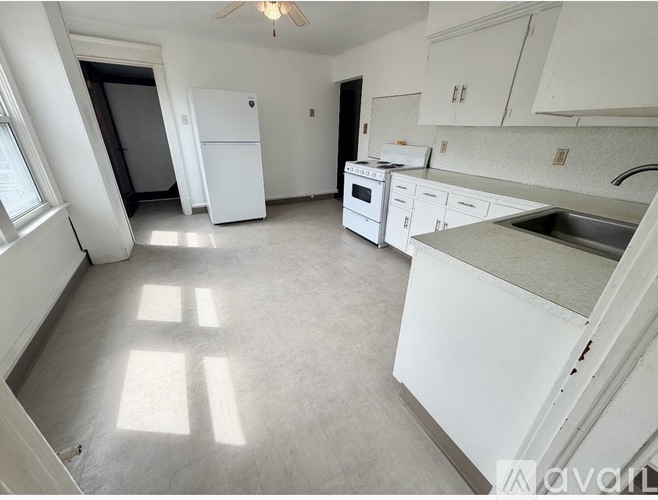 A kitchen with white appliances and cabinets is empty and sunlight is shining through the windows.