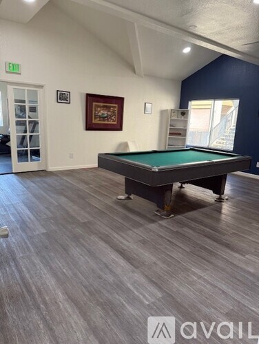 A pool table in a room with light wood flooring and a green exit sign on the wall.