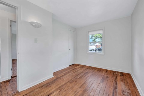 A room with wooden floors and a window showing a car and a tree outside.