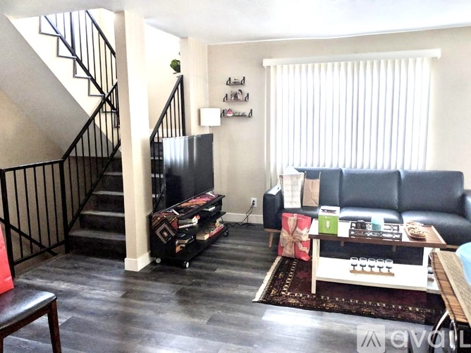 A living room with a black couch and a staircase.