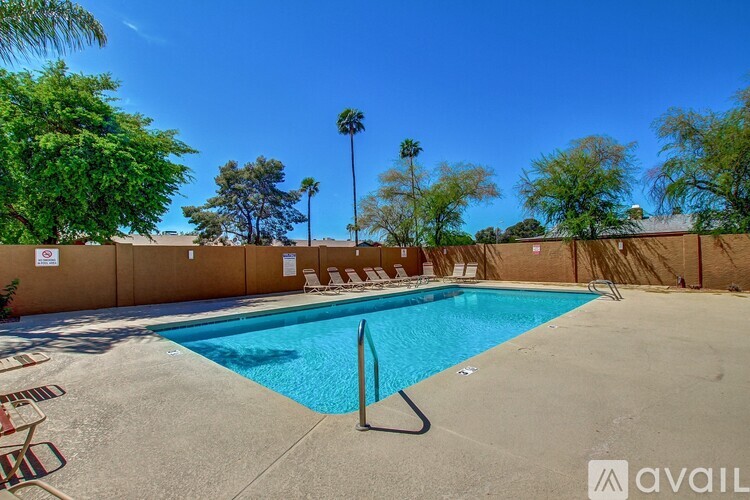 A pool surrounded by a wall with chairs and trees in the background.