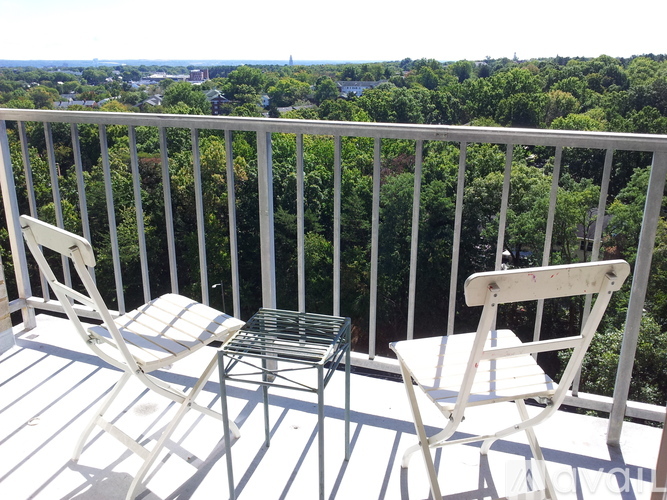 Two white chairs on a balcony with a view of trees and buildings.