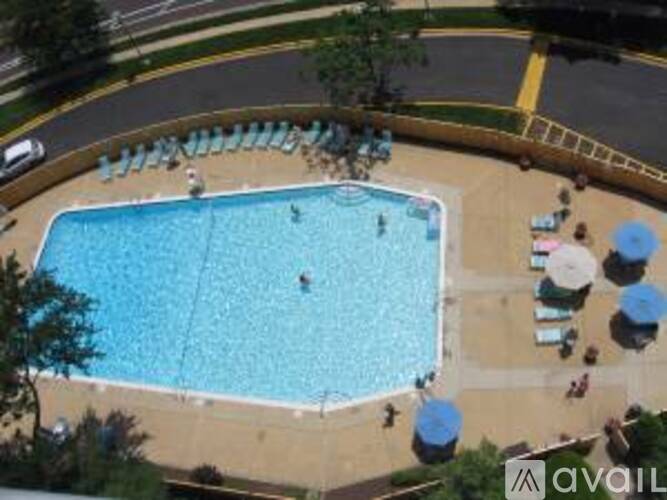 A large blue swimming pool with people in it and sun loungers around the pool.