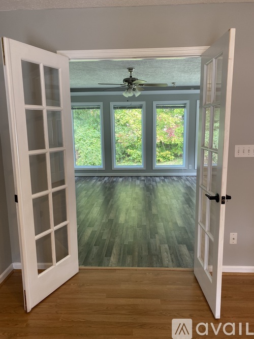 A room with a ceiling fan and a view of a garden through the windows.
