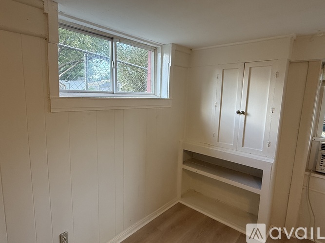 A room with a window, wooden floors, and white walls.