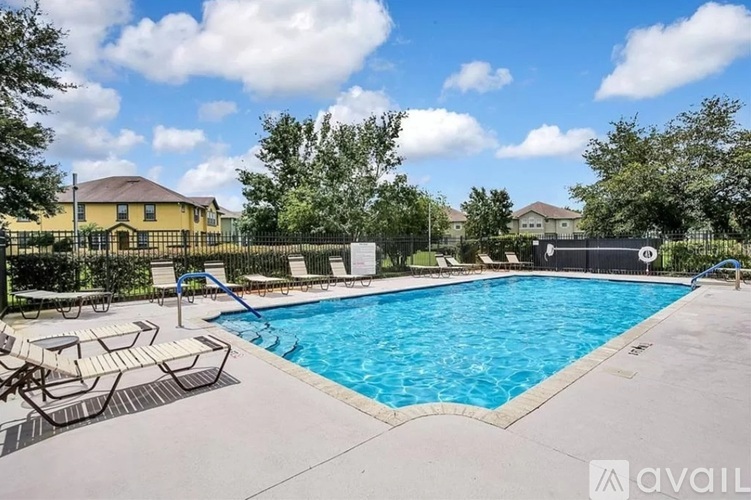 A large outdoor swimming pool surrounded by a concrete patio and lounge chairs.