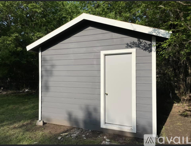 A small grey shed with a white door is situated in a grassy area.