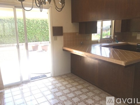 A kitchen with a brown counter and a window with a view of a hedge.