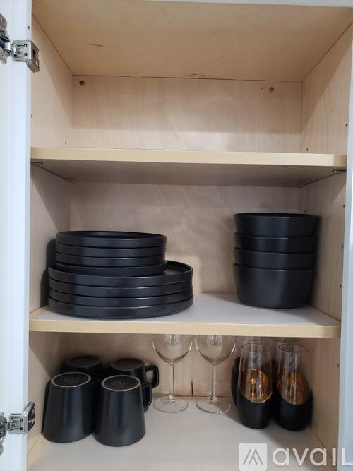 A kitchen cabinet with black dishes and wine glasses.