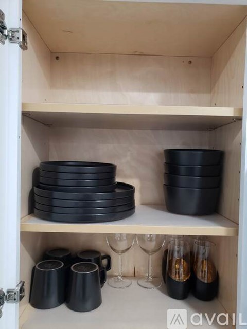 A kitchen cabinet with black dishes and wine glasses.