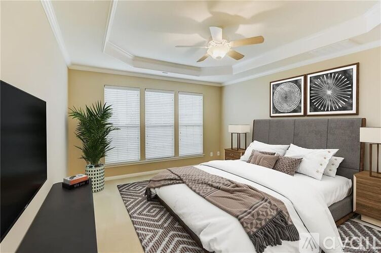 A bedroom with a large bed, a ceiling fan, and a plant.